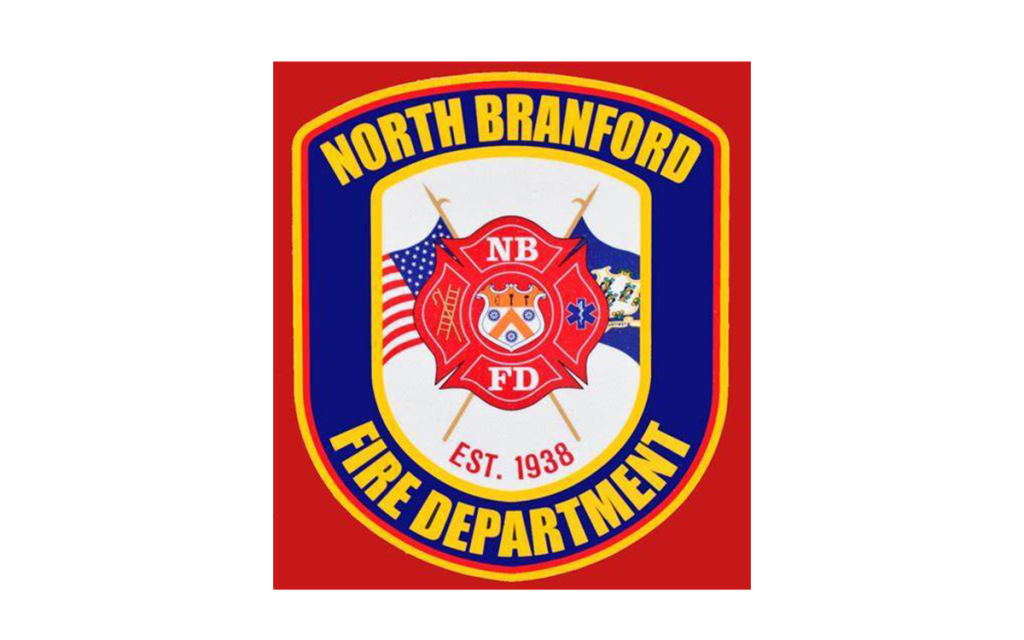 A badge with "North Branford Fire Department" and "Est. 1938" text, featuring a firefighter shield, U.S. flag, state flag, and medical symbol on a red and yellow background.